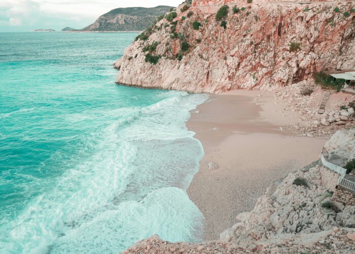 Serene view of sandy beach with waves crashing against rocky cliffs in Antalya, Türkiye.